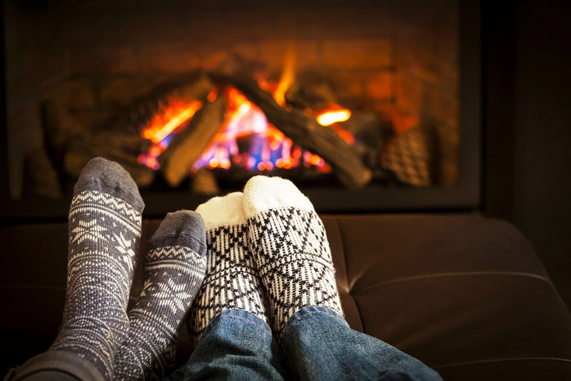 Top Hat & Tails Chimney - Stock image of feet in front of fireplace feet in front of a lit fireplace